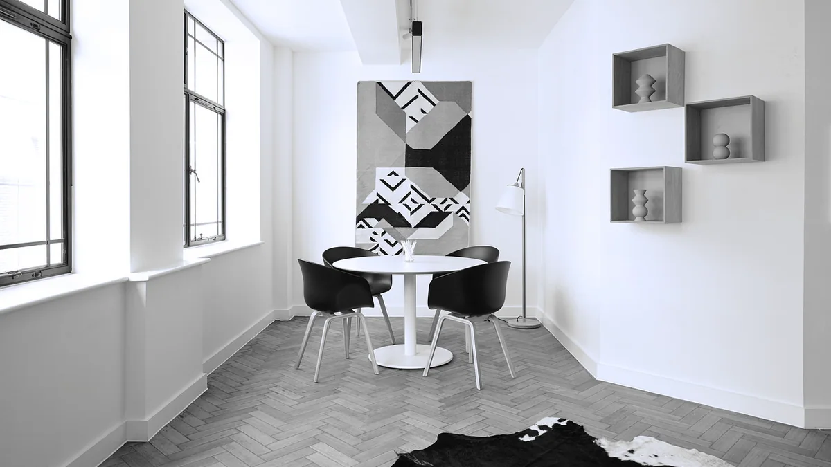A kitchen table and chairs on a herringbone floor beside a tall window.