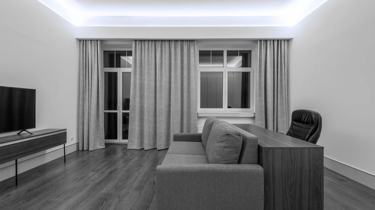A hall opening onto a sitting room, with curtains drawn back from a tall window.